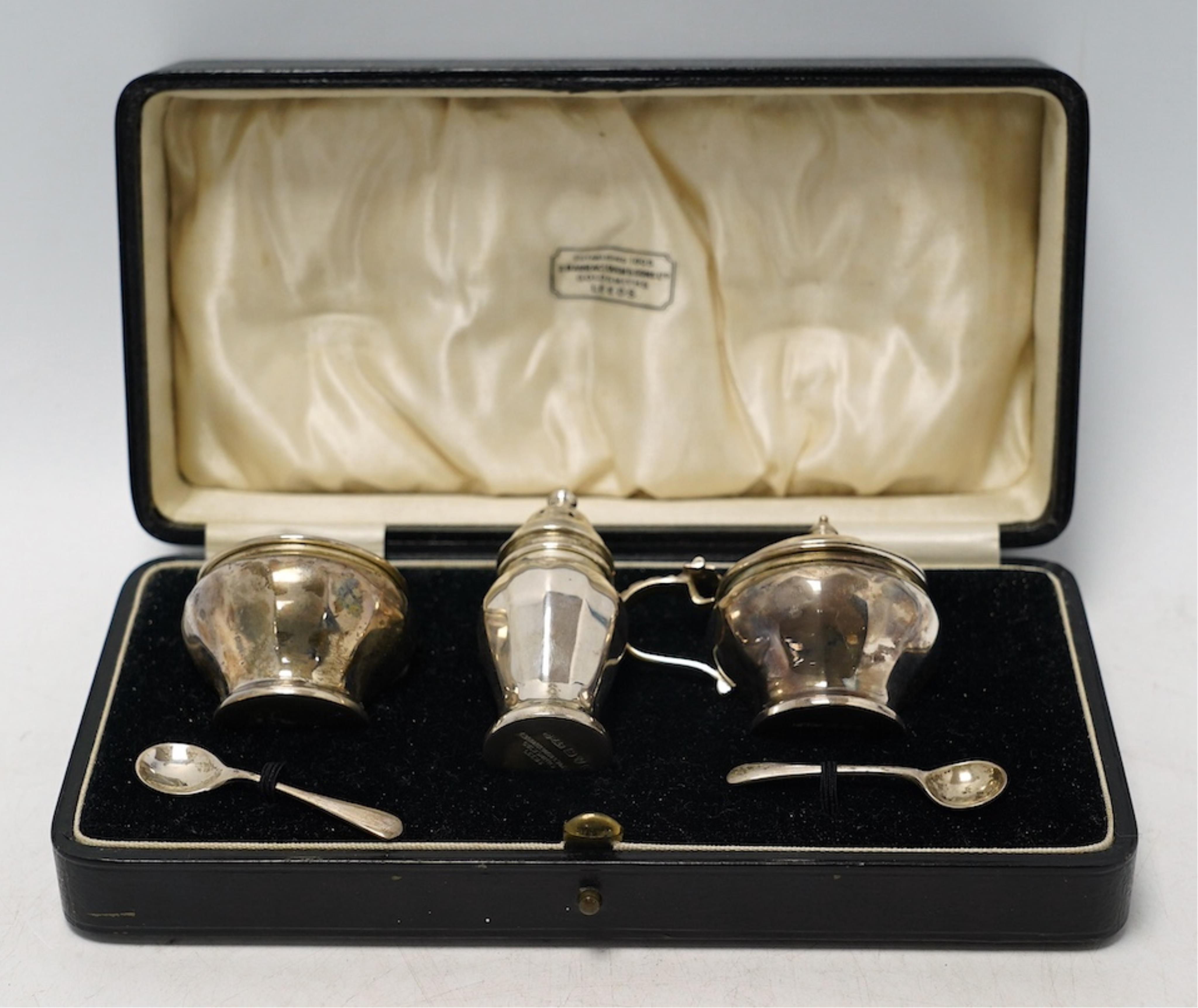 A cased George V silver three piece condiment set, Z. Barraclough & Sons, Chester, 1931, with two associated silver spoons. Condition - fair